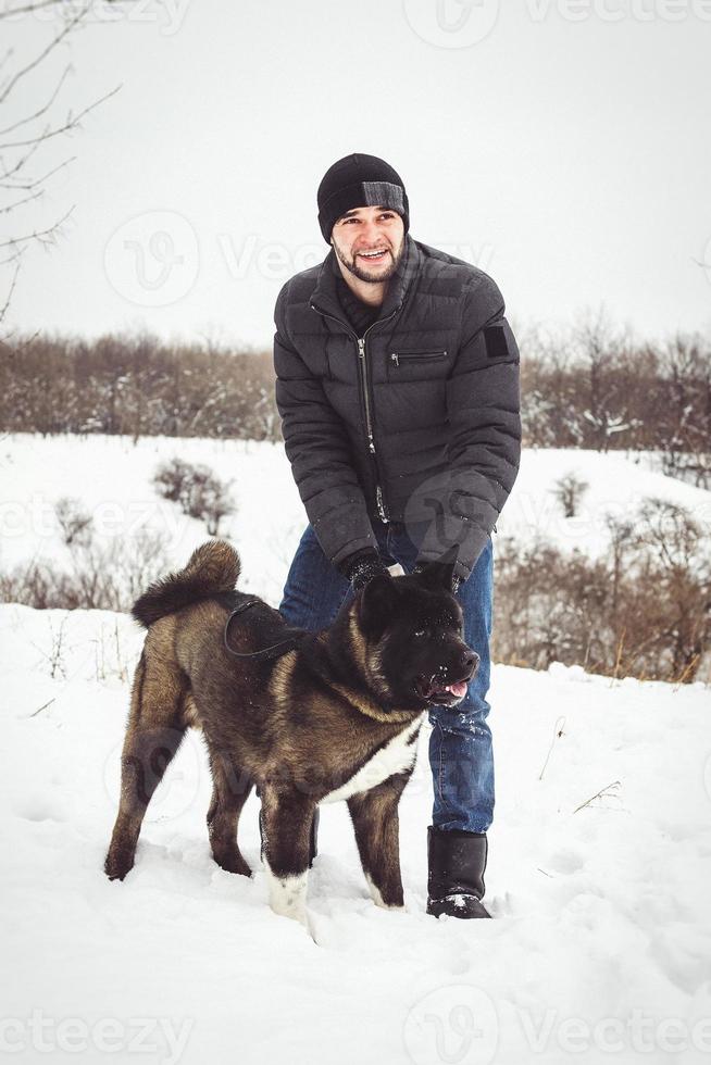 en man i en jacka och en stickad hatt går med en amerikansk akitahund foto