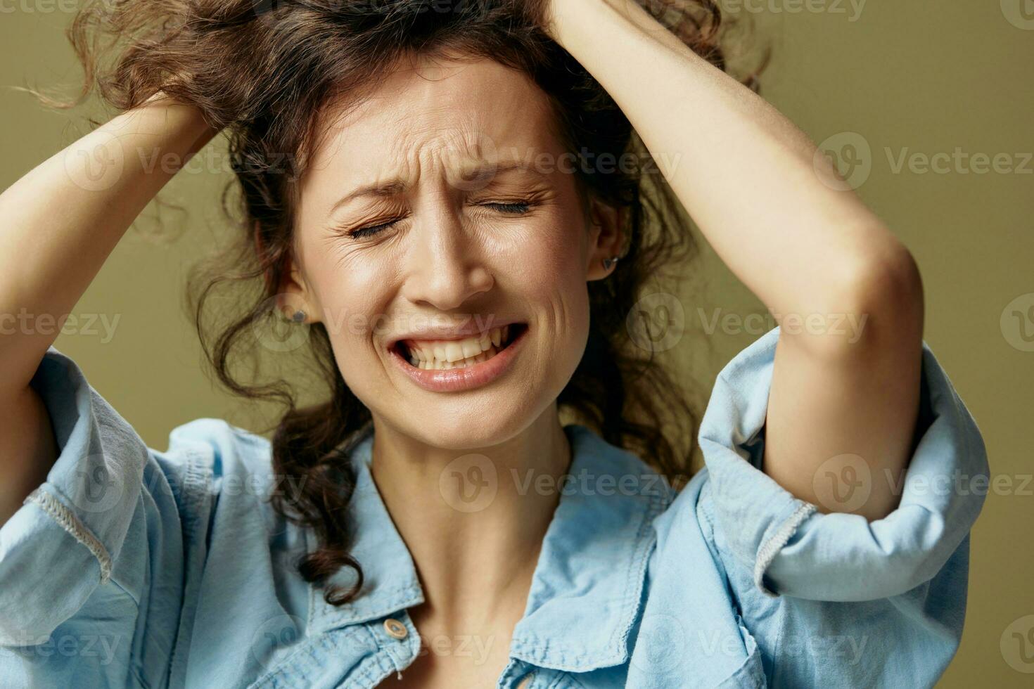 lidande skrikande gråt lockigt skön kvinna i jeans tillfällig skjorta Rör huvud Framställ isolerat på över oliv grön pastell bakgrund. varelse själv. människor livsstil känslor begrepp. kopia Plats foto