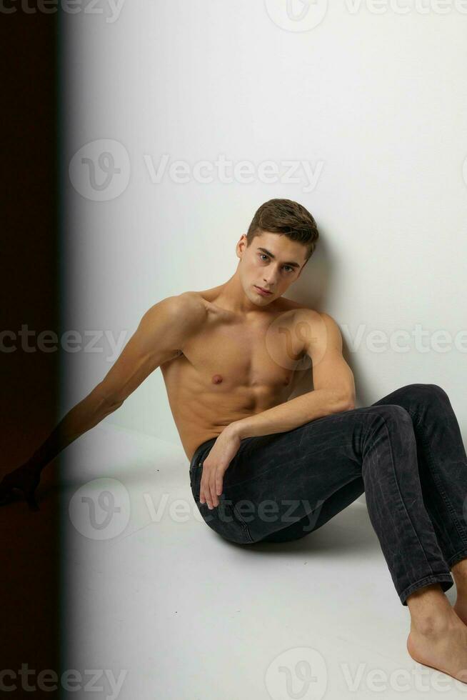 stilig man i svart byxor sitter på de golv naken torso studio attraktivitet foto