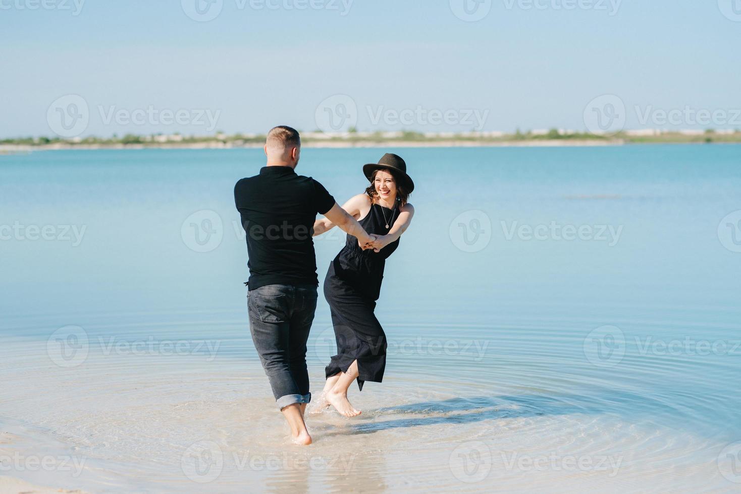 ungt par en kille med en flicka i svarta kläder går på den vita sanden foto