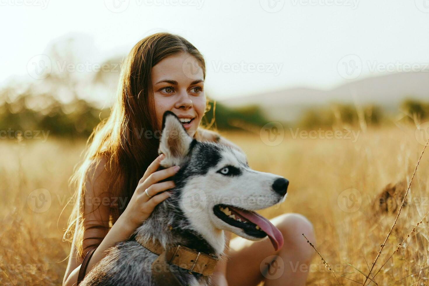 kvinna och henne hes hund lyckligt promenad genom de gräs i de parkera leende med tänder falla solnedgång promenad med sällskapsdjur, resa med en hund vän foto