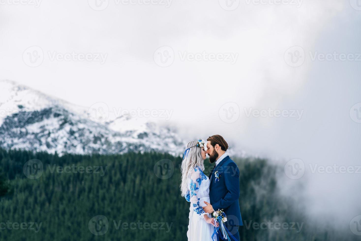 brudgummen i en blå kostym och bruden i vitt i bergen karpaterna foto