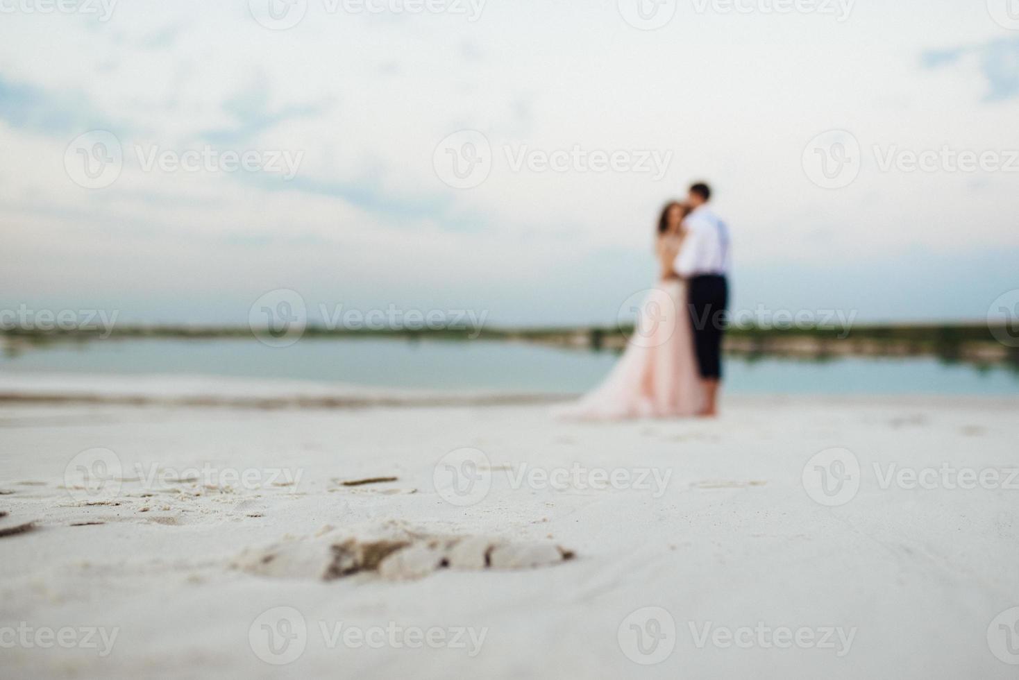 ungt par en kille i svarta byxor och en flicka i en rosa klänning går längs den vita sanden foto