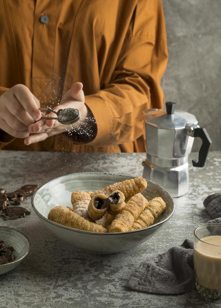 person som sätter pulveriserat socker på tequenos maträtt foto