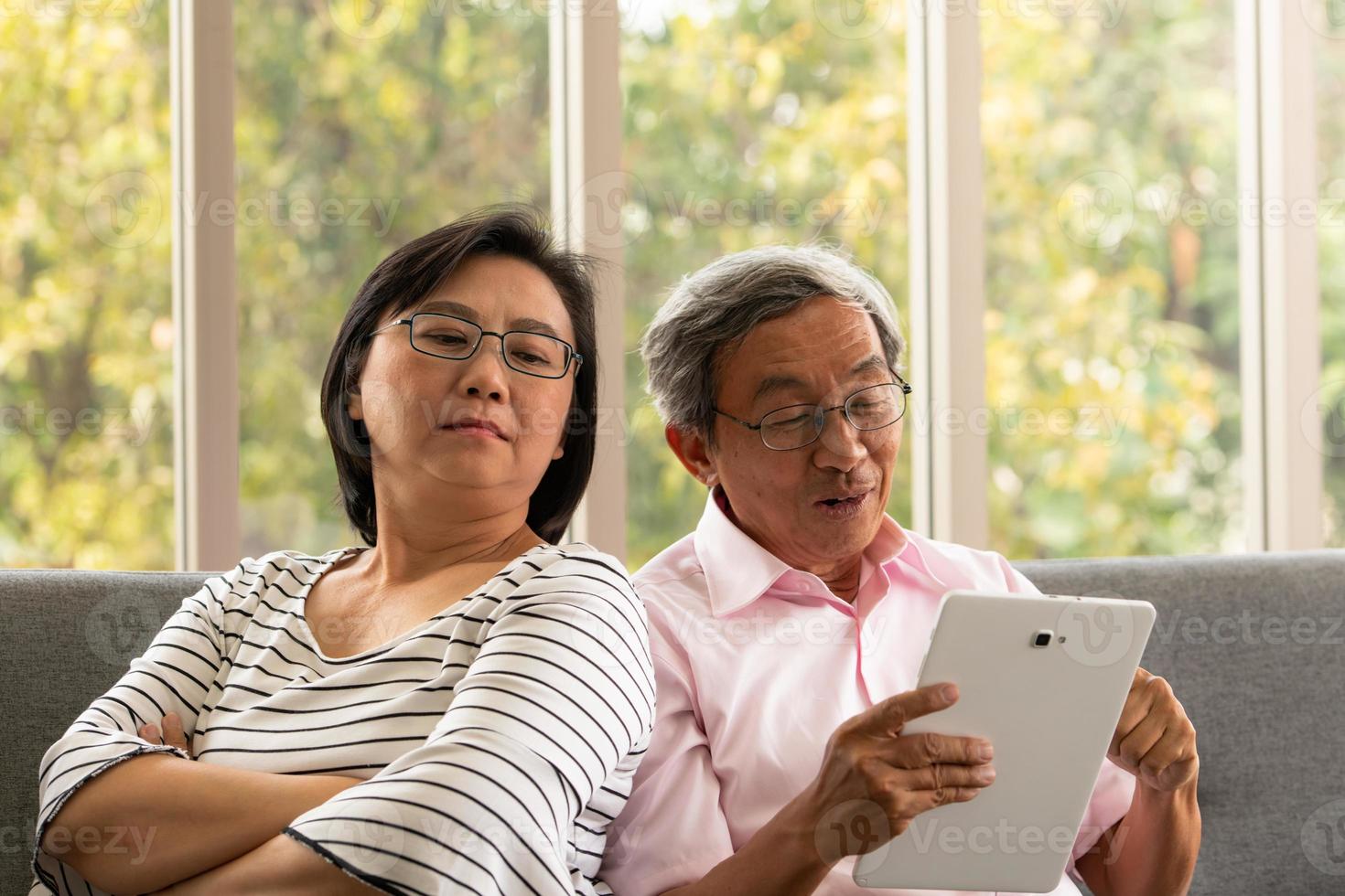 senior asiatisk man och kvinna kopplar av på semester i den naturliga vardagsrumsbakgrunden med modern teknik foto