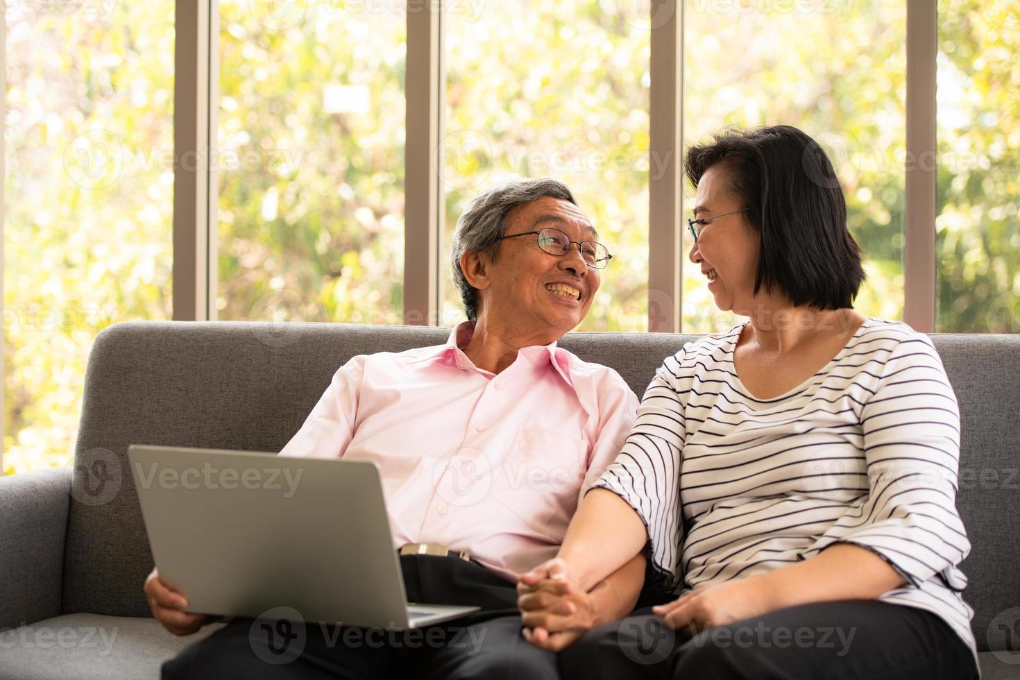 senior asiatisk man och kvinna kopplar av på semester i den naturliga vardagsrumsbakgrunden med modern teknik foto