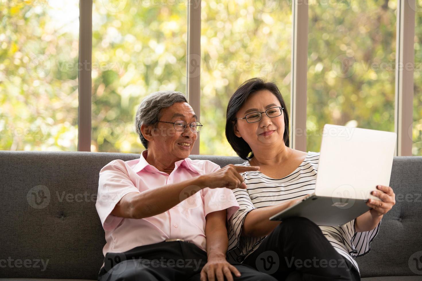 senior asiatisk man och kvinna kopplar av på semester i den naturliga vardagsrumsbakgrunden med modern teknik foto