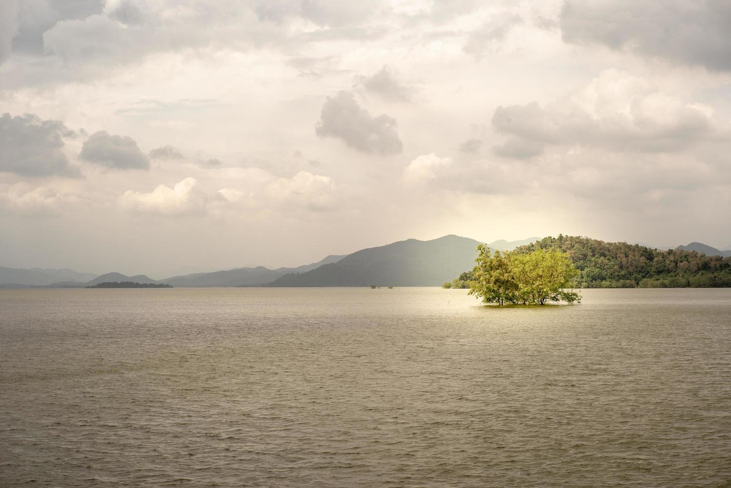 liggande horisontell linje av oändliga berg och stor sjö med träd som växer i vattnet. vatten i den naturliga dammen vid phetchaburi foto