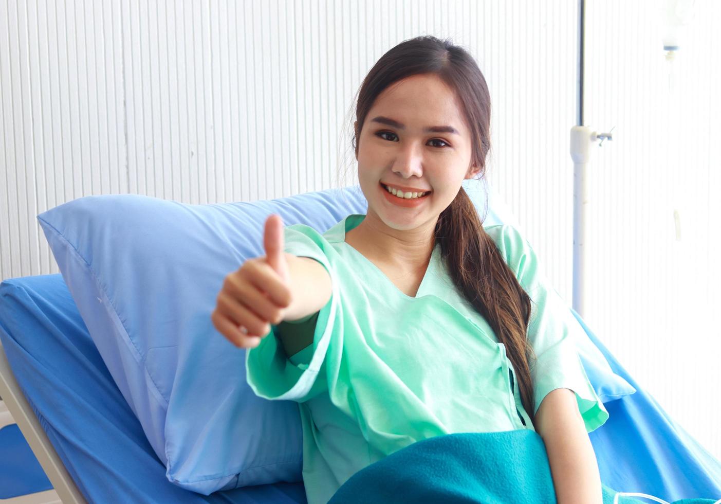 vacker asiatisk kvinna sitter på en sjukhussäng med ett leende ansikte foto
