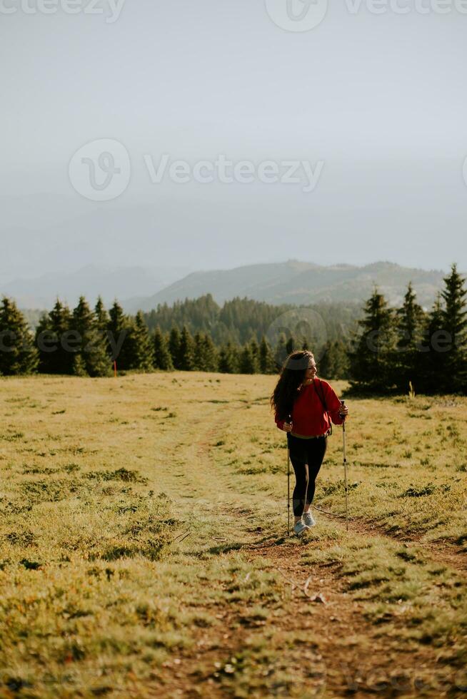 ung kvinna gående med ryggsäck över grön kullar foto