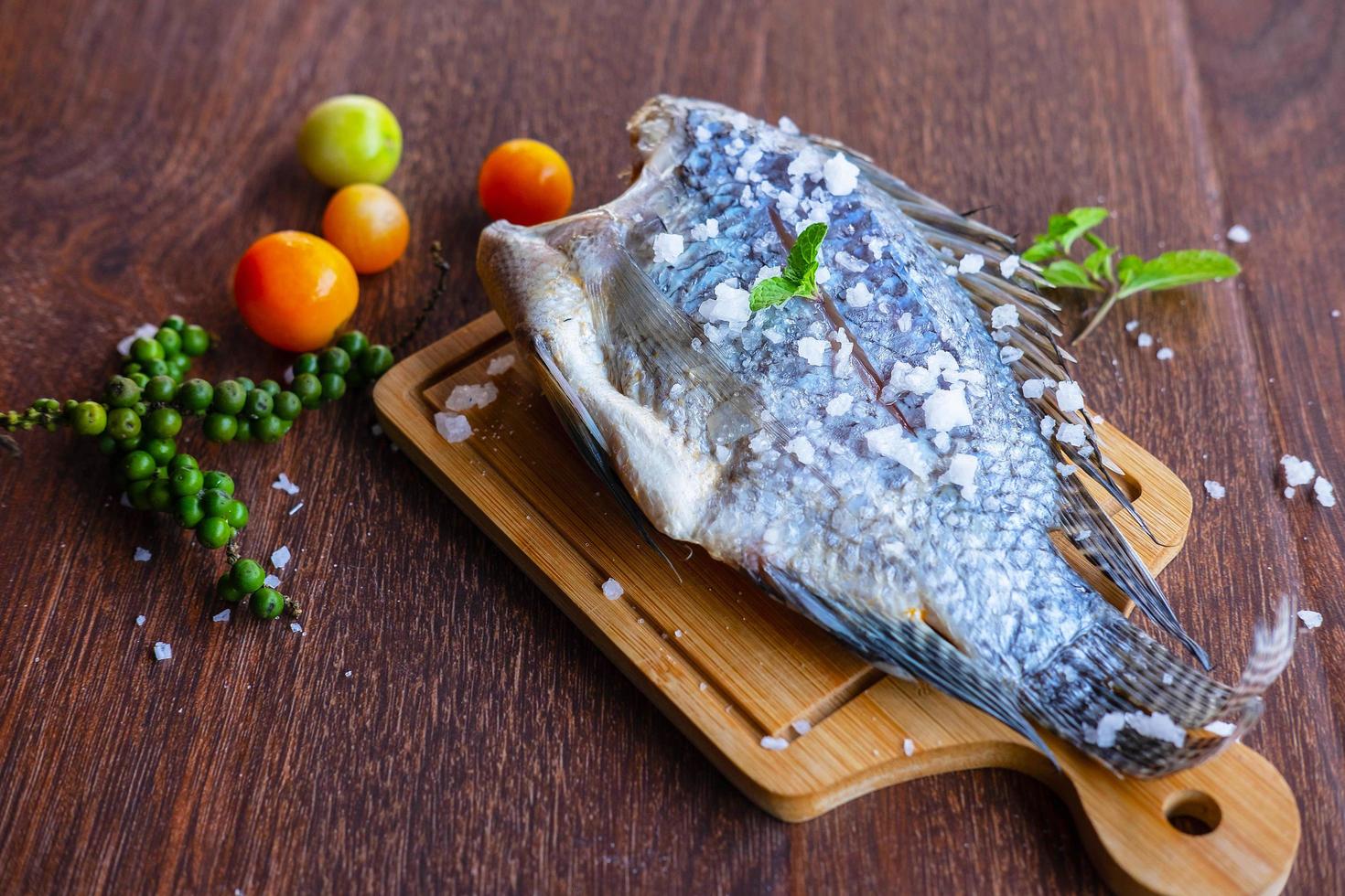 läcker färsk fisk på mörk bakgrund. fisk med aromatiska örter, diet eller matlagningskoncept. foto