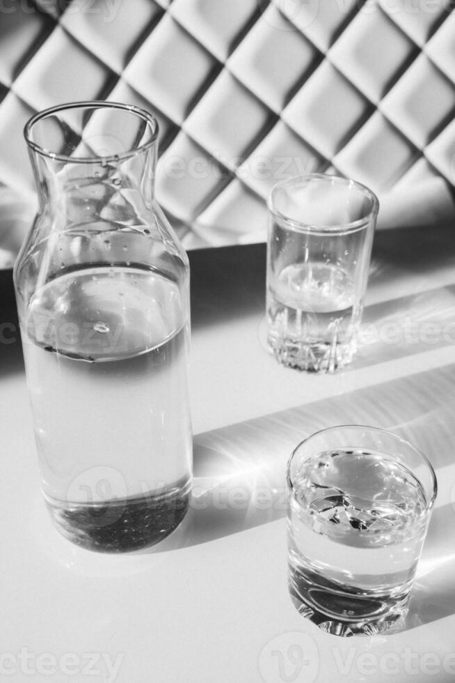 vatten i glasögon och i en vas på vit stål. skuggor, hård ljus. foto