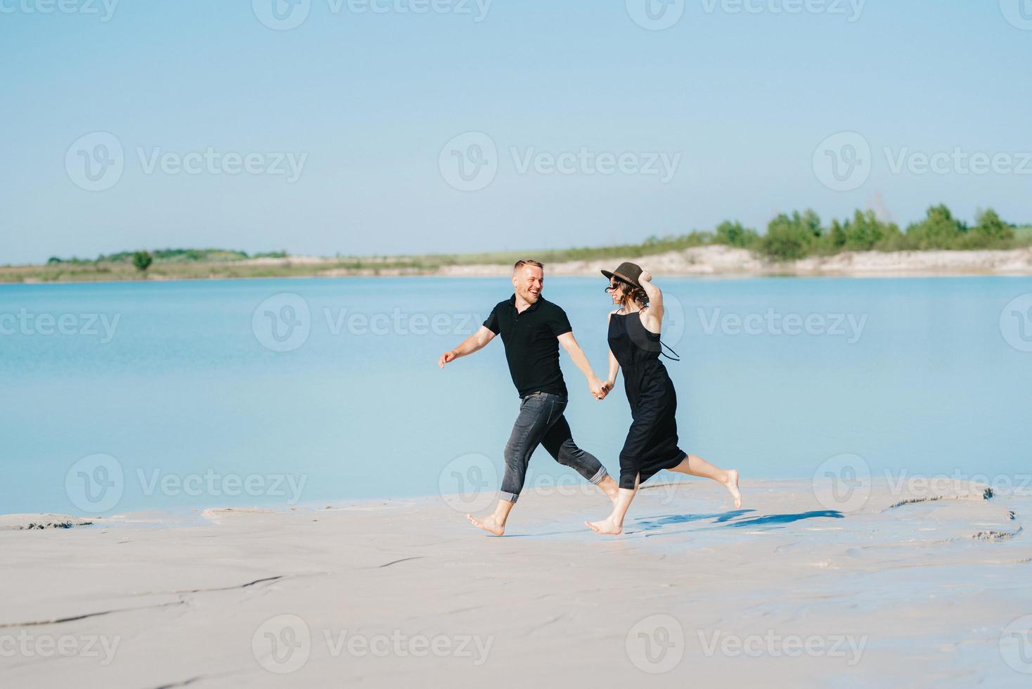 ungt par en kille med en flicka i svarta kläder går på den vita sanden foto