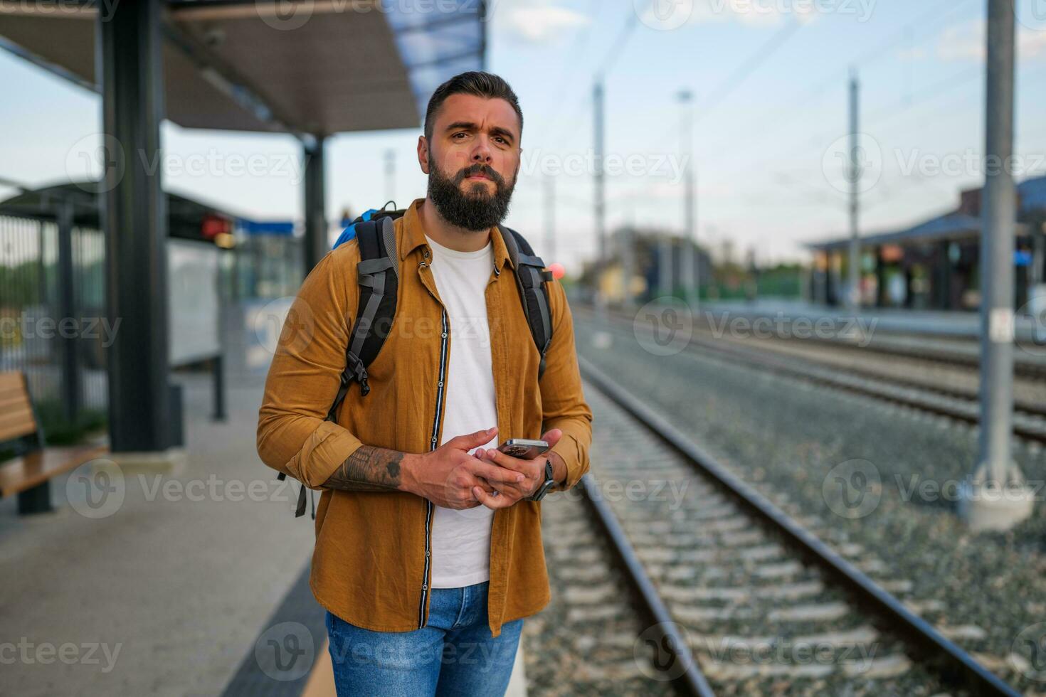 vuxen man är stående på järnväg station och väntar för ankomst av tåg. foto