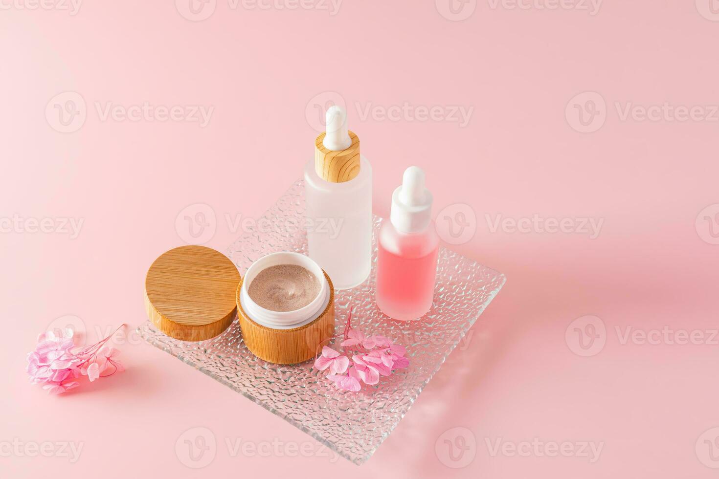 kropp skrubba i ett öppen bambu burk och två kosmetika i matt vit flaskor med en dropper för naturlig ansikte och kropp hud vård. rosa bakgrund. foto