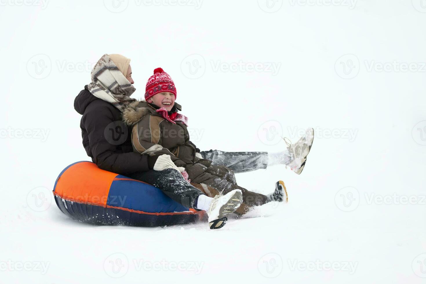vinter- underhållning. glad människor i värma kläder är ridning ner en snöig berg på en kälke. foto