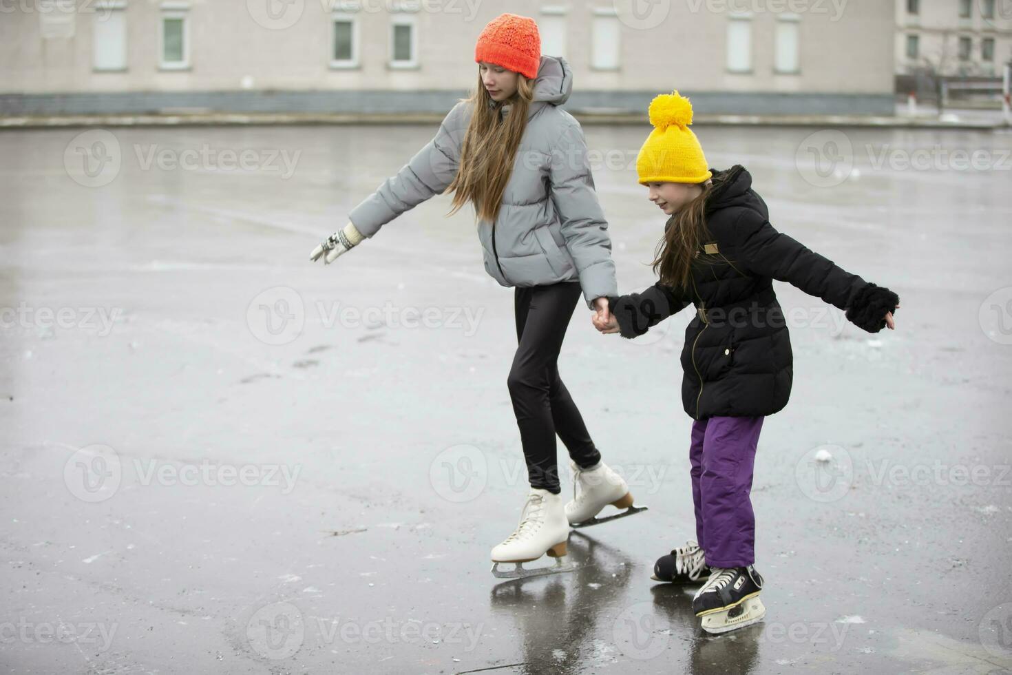 barn is skridskoåkning på de stad skridskoåkning rink. de äldre syster lär de yngre ett till skridsko. foto