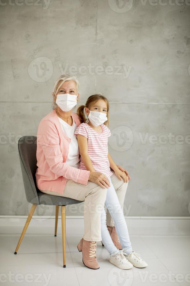 vertikal sikt av en mormor i en stol med barnbarn som bär masker foto