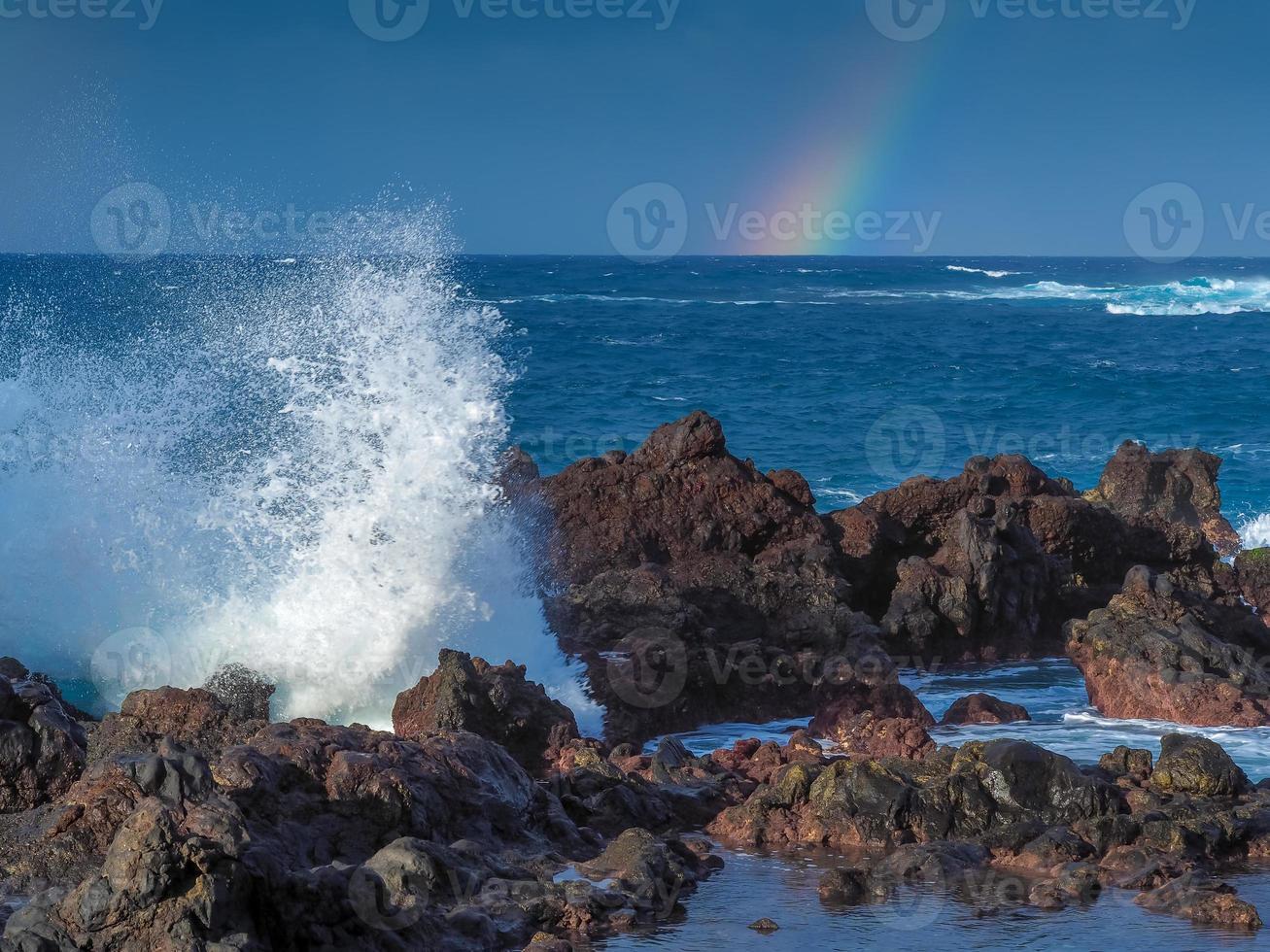 vågor som stänker på stenar och en regnbåge vid Puerto de la Cruz teneriffa kanarieöarna foto