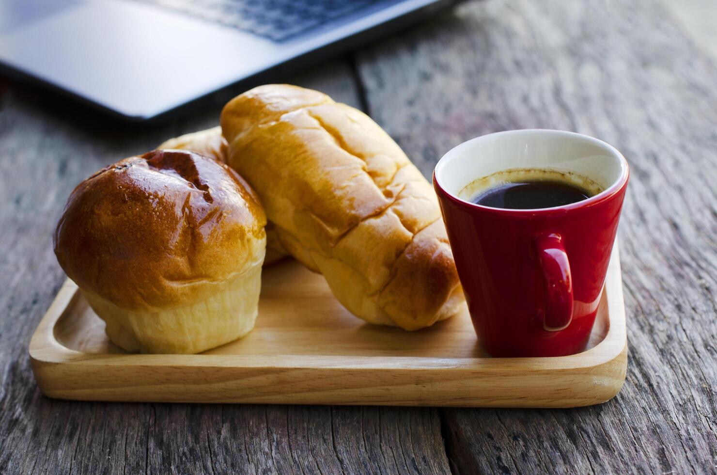 röd kaffekopp och läckra bullar på träplatta med bärbar dator på träbordbakgrund foto