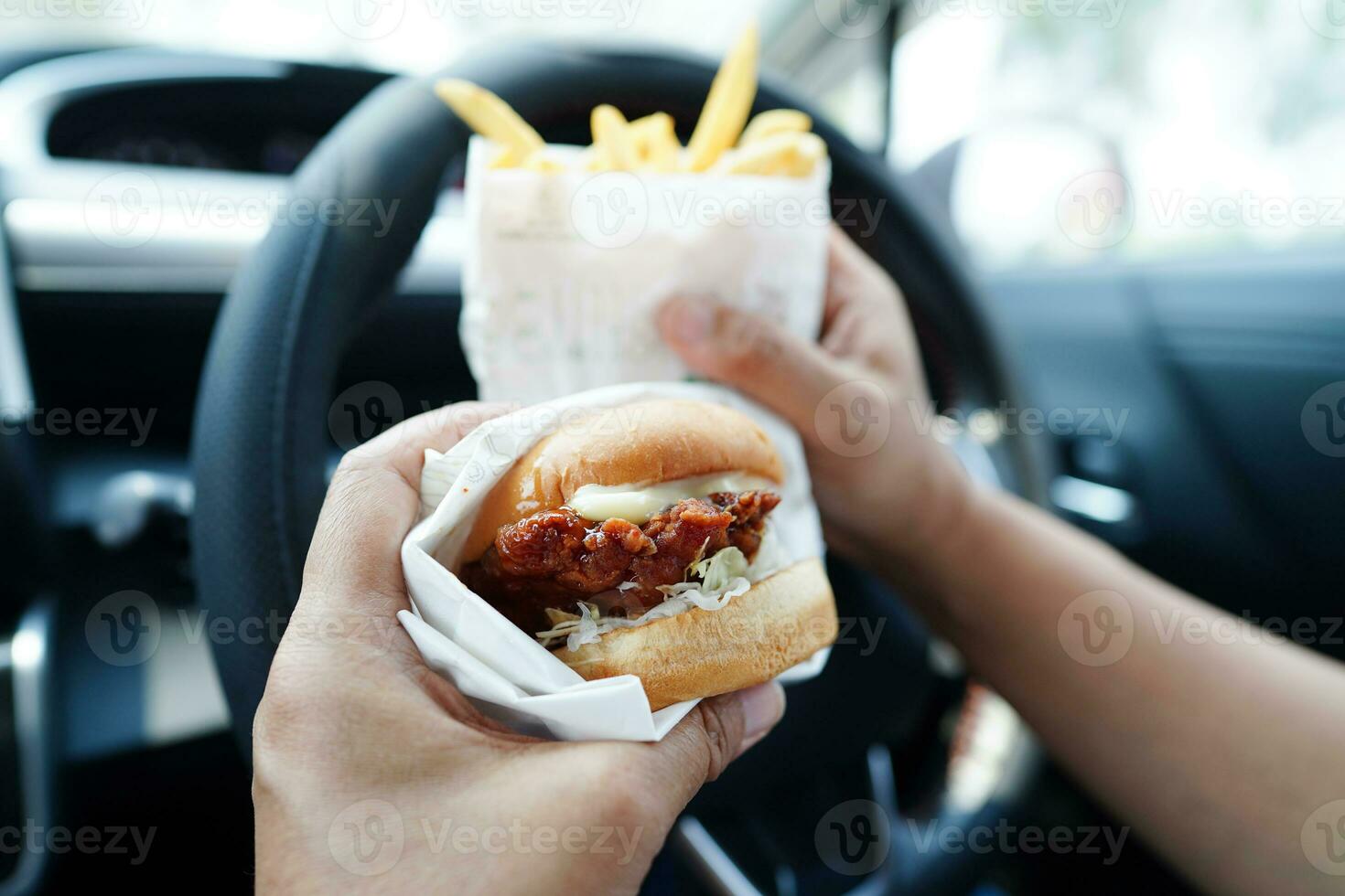 asiatisk kvinna förare håll och äta hamburgare och franska frites i bil, farlig och risk ett olycka. foto