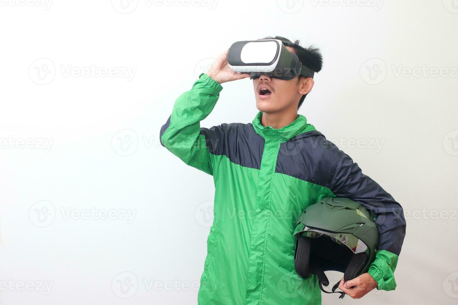 porträtt av asiatisk uppkopplad taxi förare bär grön jacka och innehav en hjälm medan använder sig av virtuell verklighet eller vr och pekande. isolerat bild på vit bakgrund foto