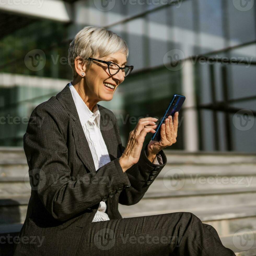 mogna affärskvinna Sammanträde i främre av företag byggnad och meddelandehantering på smartphone. foto