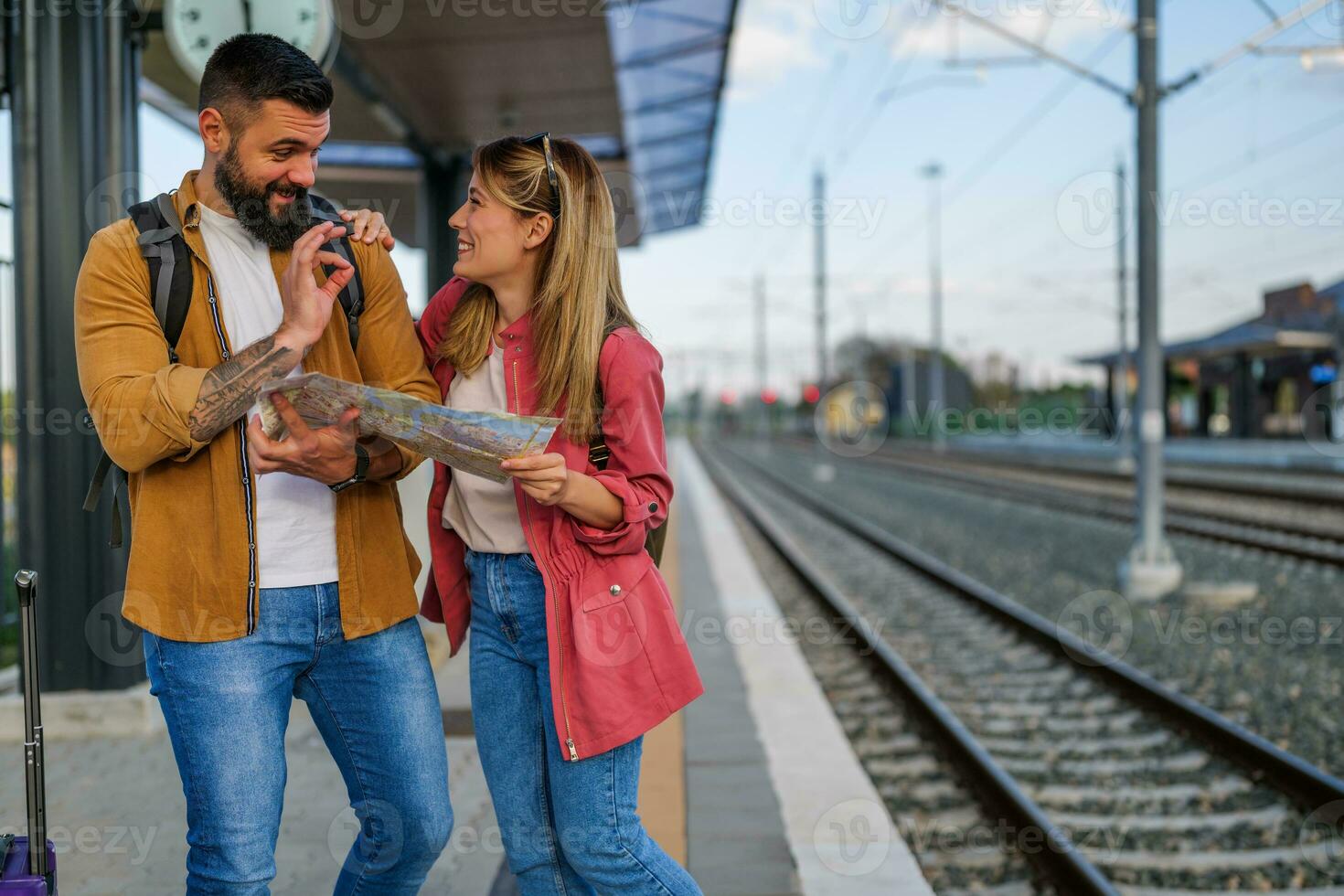 Lycklig par är stående på järnväg station och väntar för ankomst av deras tåg. de är ser på Karta. foto