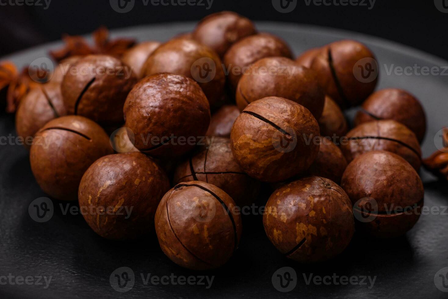 utsökt rostad macadamia nötter i skal på en mörk texturerad bakgrund foto