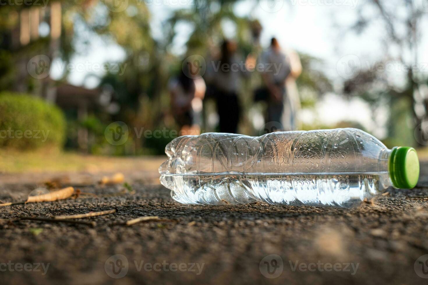 närbild klar plastflaska vattendrink med en grön keps på vägen i parken vid suddig bakgrund, skräp som är kvar utanför soptunnan, skräp på marken i trädgården foto