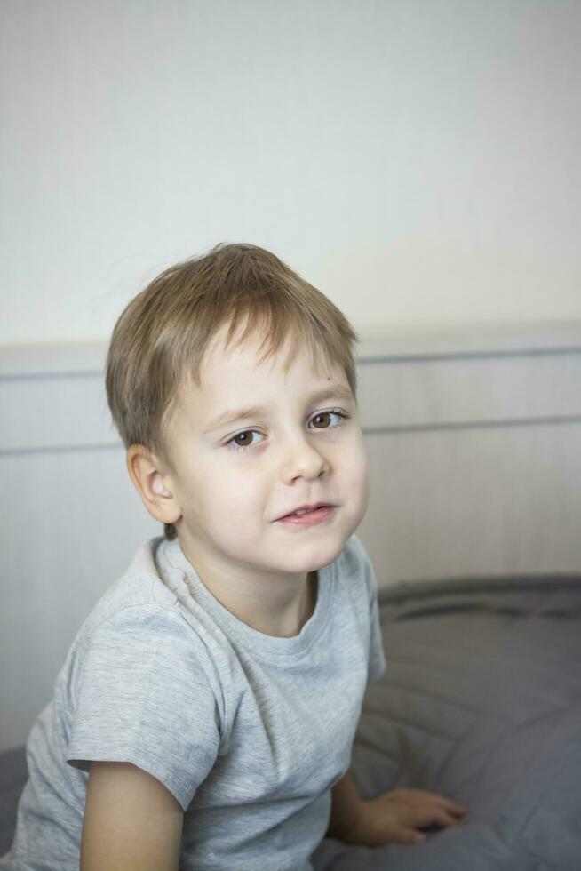 en Foto av en stilig pojke i en grå t-shirt ser på de kamera. porträtt i en ljus rum. naturlig, inte iscensatt fotografi.