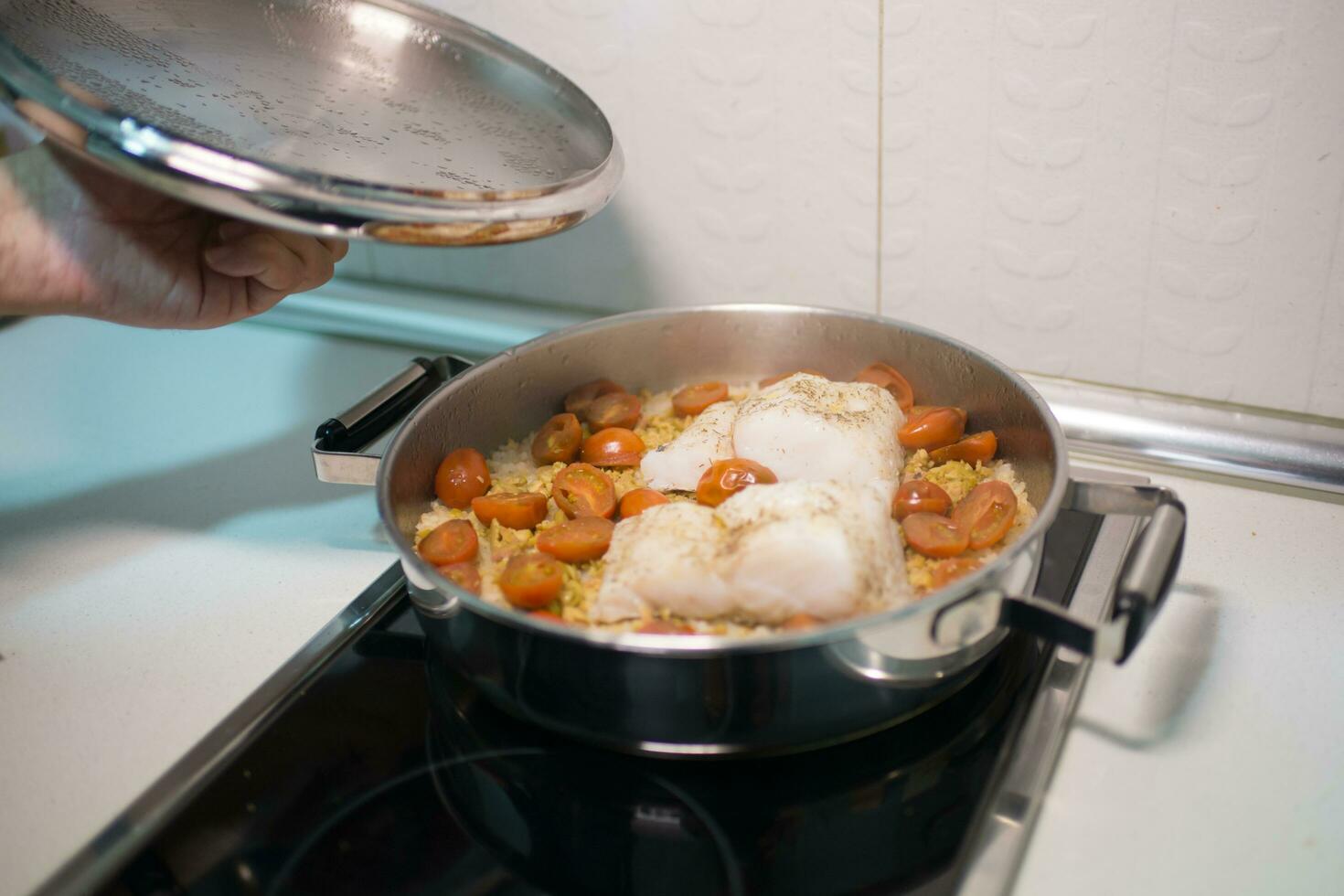 mänsklig hand öppning en matlagning pott med ris, kummel och körsbär tomater foto