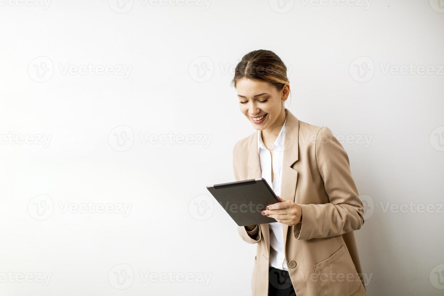 ung kvinna som rymmer den digitala minnestavlan vid den vita väggen i modernt kontor foto