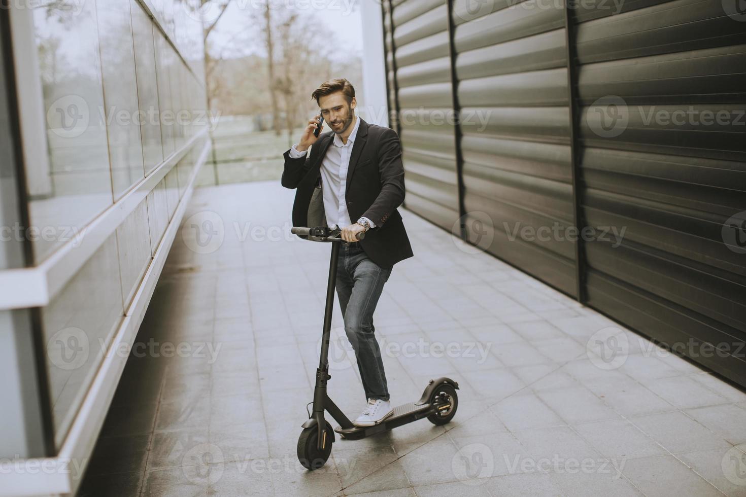 ung affärsman som använder mobiltelefonen på elektrisk skoter foto