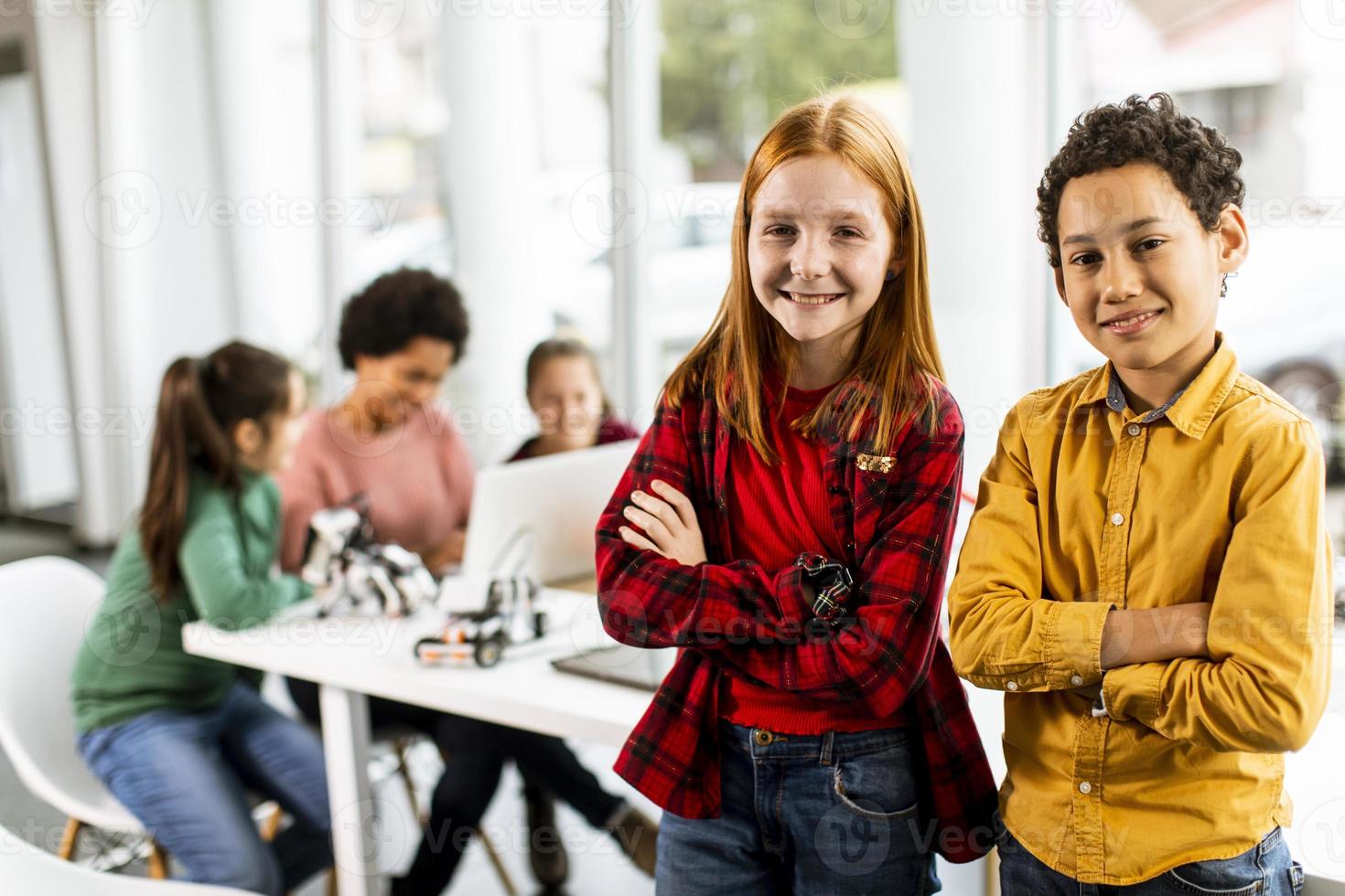 bästa vänner som står framför barn som programmerar elektriska leksaker och robotar i klassrummet för robotik foto