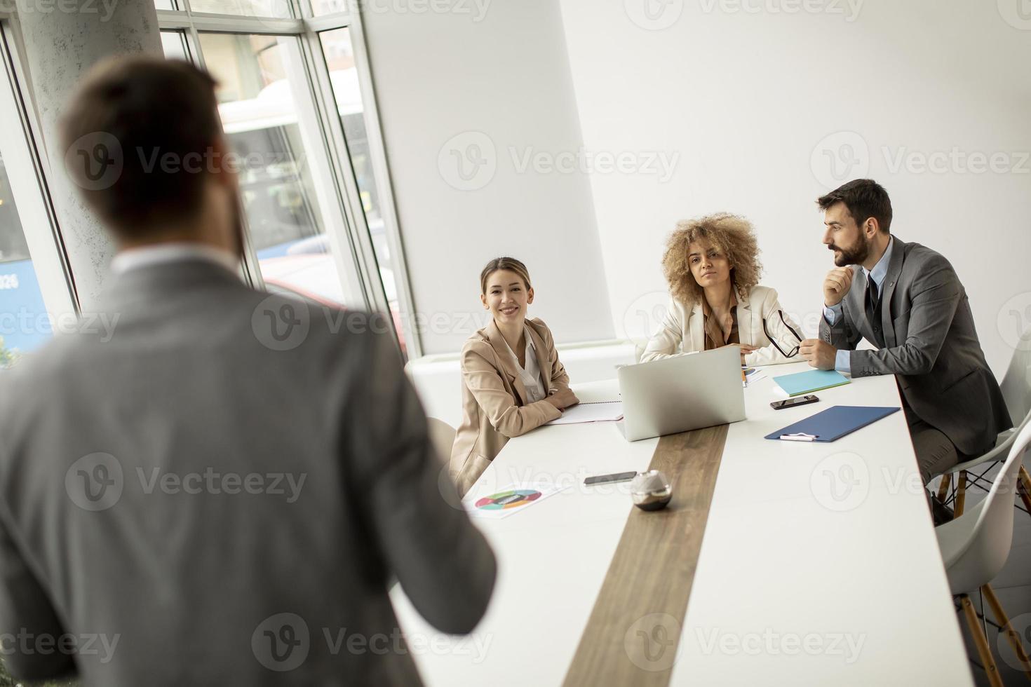 grupp unga affärsmän som arbetar och kommunicerar medan de sitter vid kontorsdisken tillsammans foto