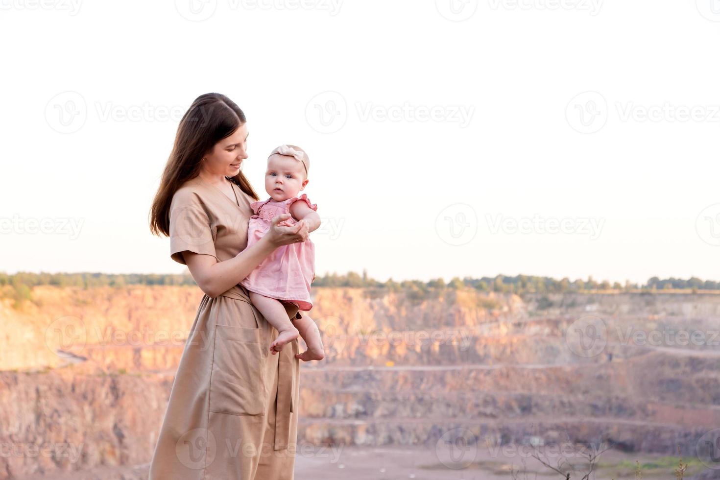 lycklig ung mamma håller sin unga baby dotter i armarna utomhus foto