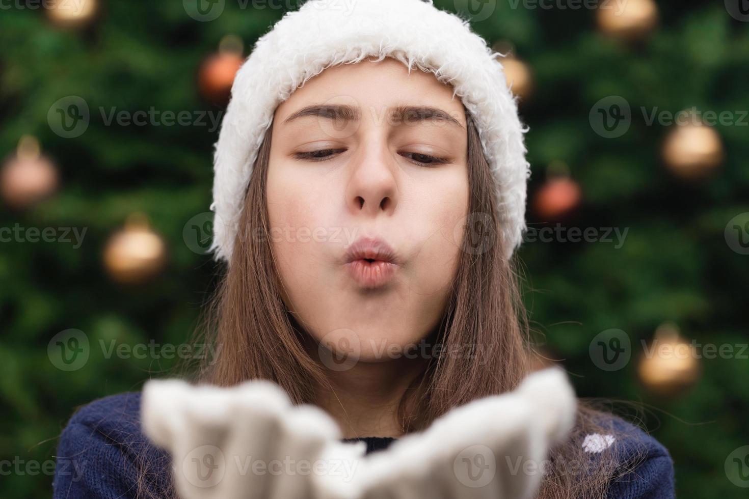 jul härlig kvinna som blåser en kyss mot dig mot julgranbakgrund foto