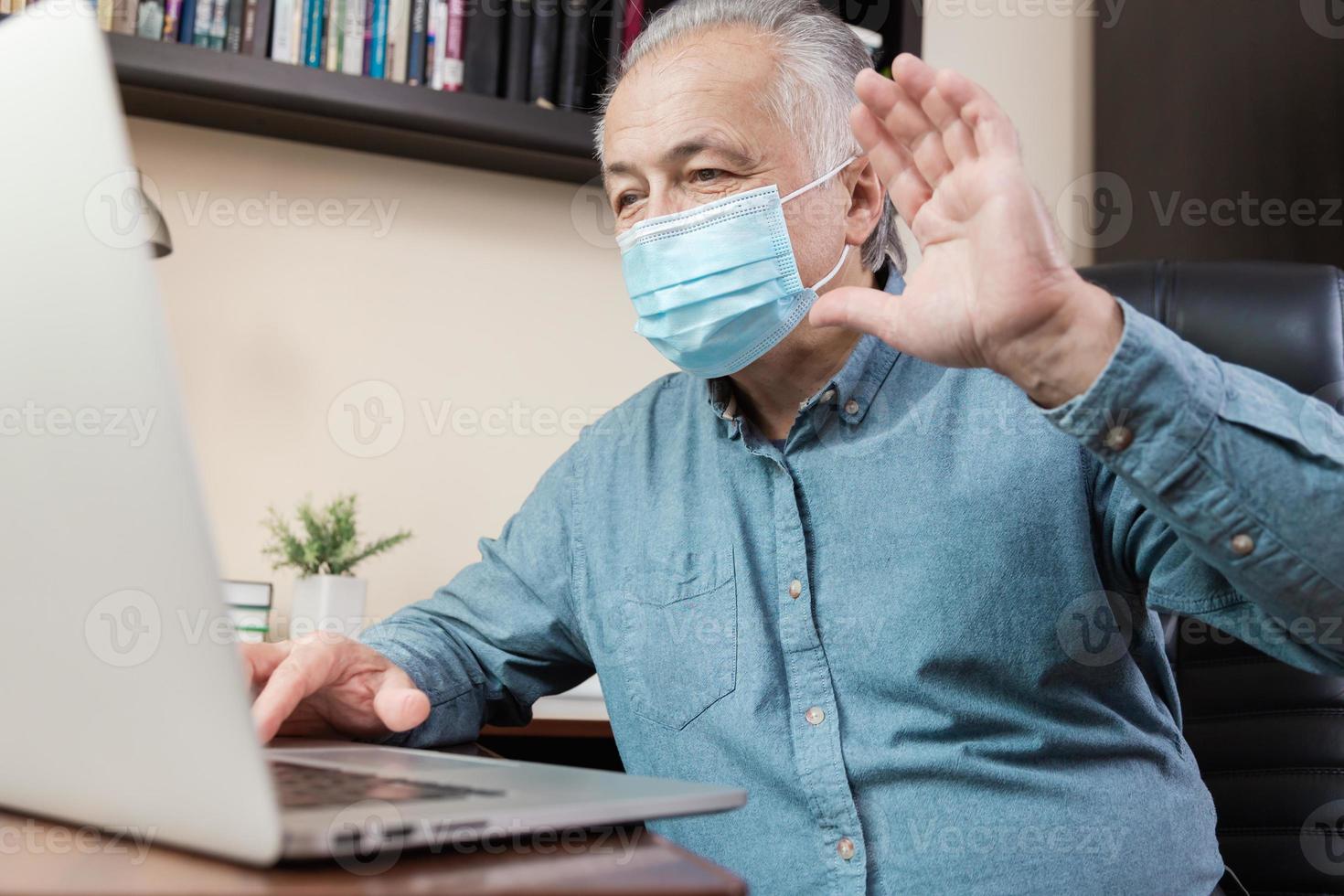 äldre man i ansiktsmask som arbetar eller kommunicerar på bärbar dator hemma foto