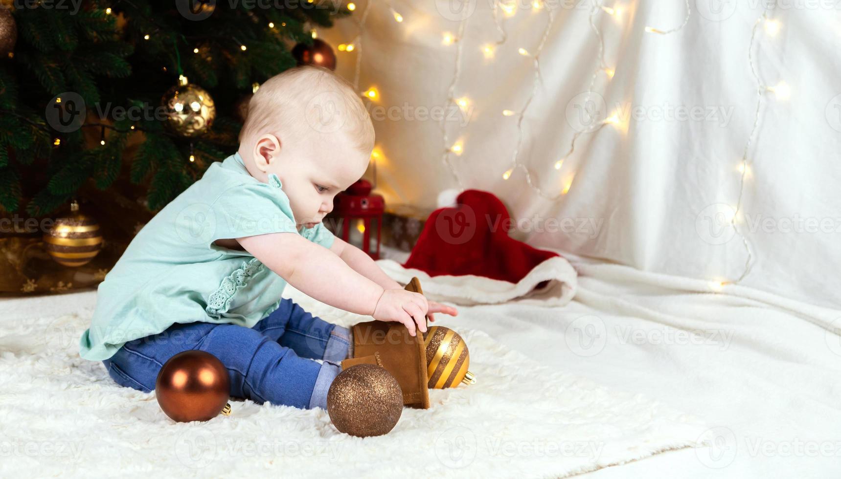 baby i jeans och skor sitter nära ett julgran foto