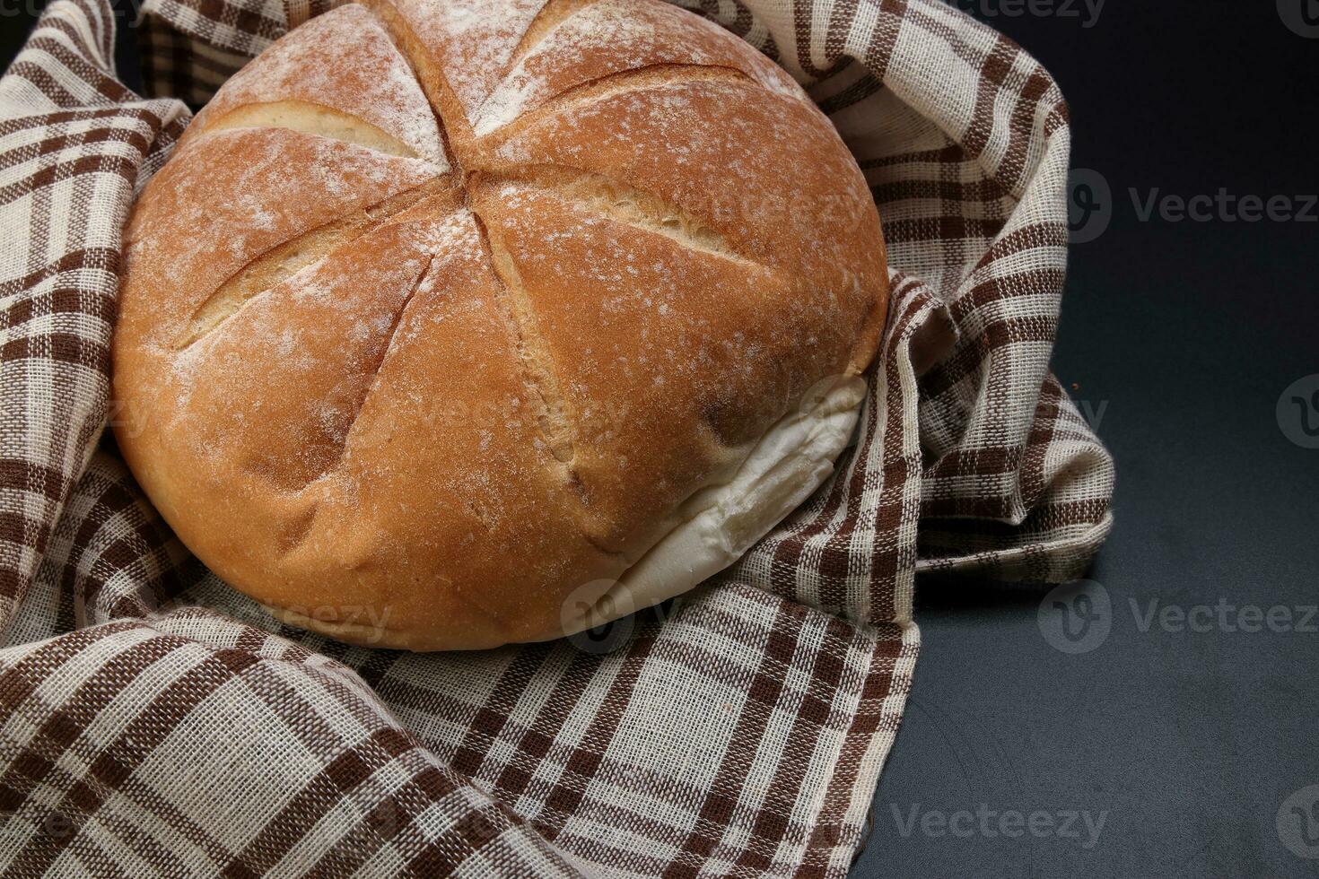 färsk bakad runda bröd limpa insvept i rutig kök tyg servett handduk över svart bakgrund foto
