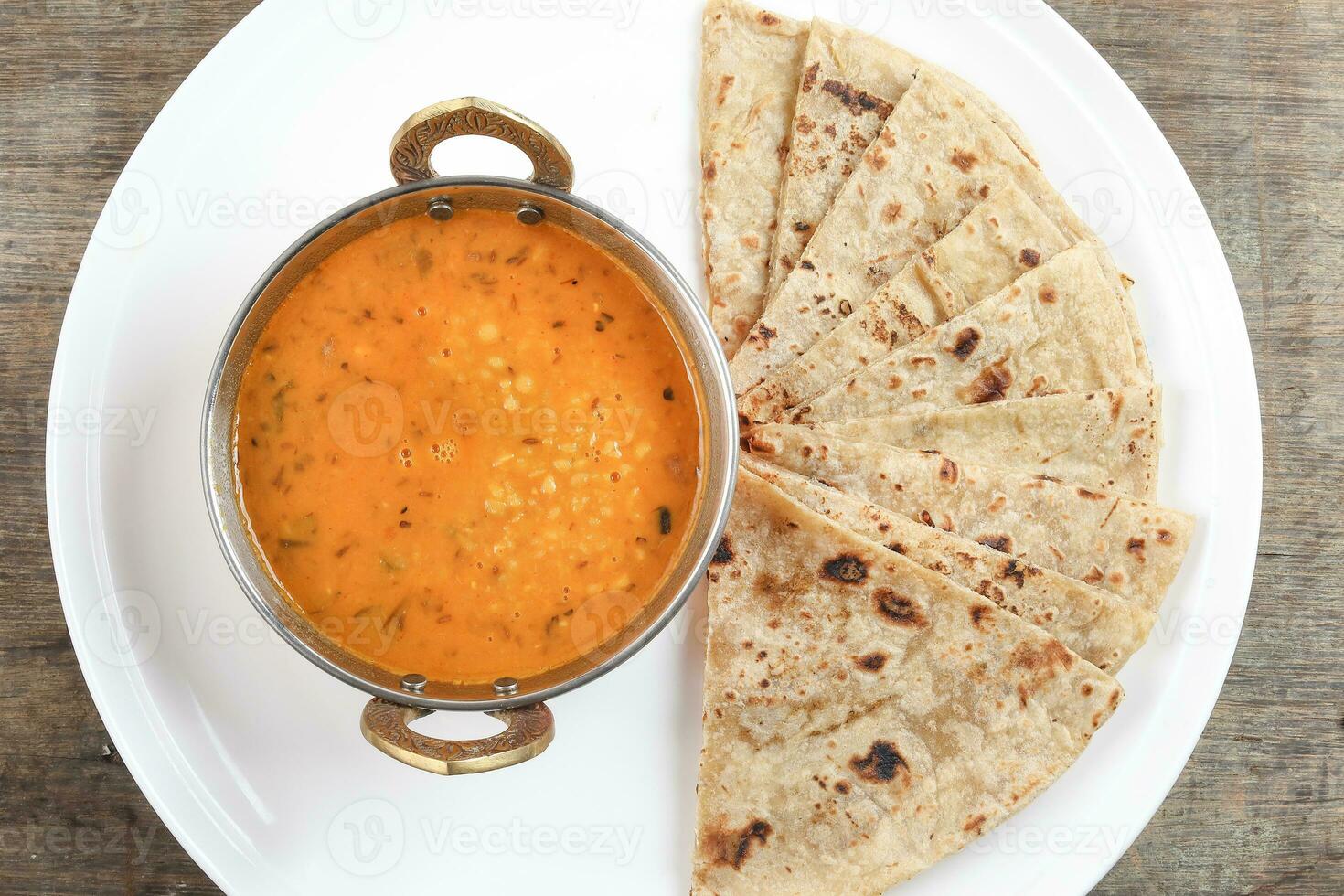 handgjort platt bröd chapati och dal tadka fritera i mässing skål panorera på vit tallrik rustik trä- bakgrund foto