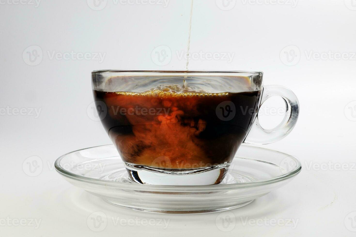 mörk kaffe poring vit mjölk droppande stänk skugga flytande virvla runt i glas kopp fat på vit bakgrund foto