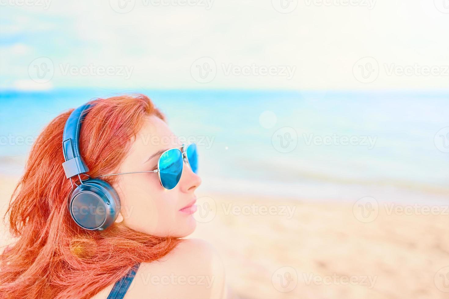 vacker kvinna i solglasögon som lyssnar på musik på stranden foto
