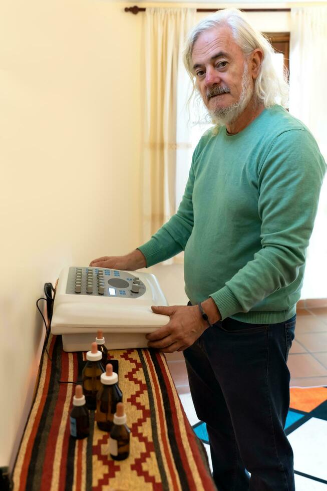 äldre man med vit hår och skägg utför en diagnos med en radion maskin. alternativ medicin behandling. foto