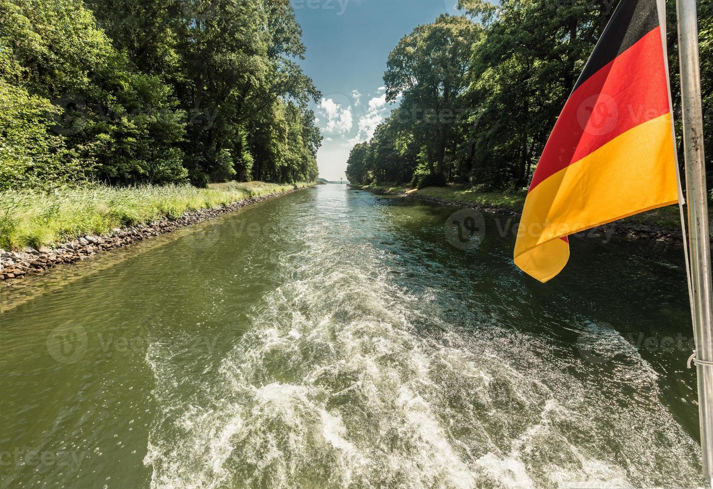 drivaxel av en båt på en kanalpassage med viftande tysklands flagga foto