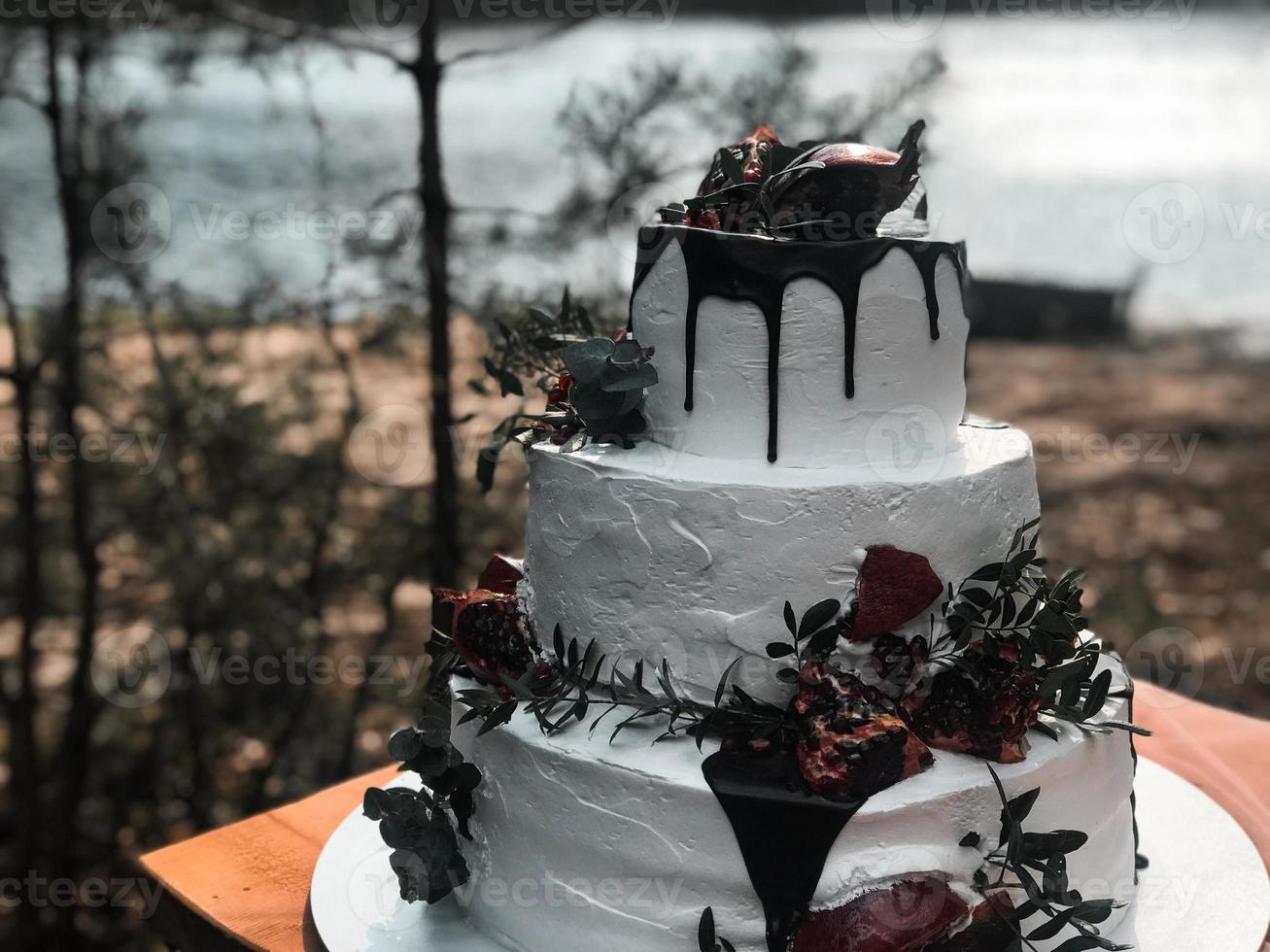 vackra tre nivåer vit kräm bröllopstårta med granatäpple frukt och färska blommor på bordet och ljus foto