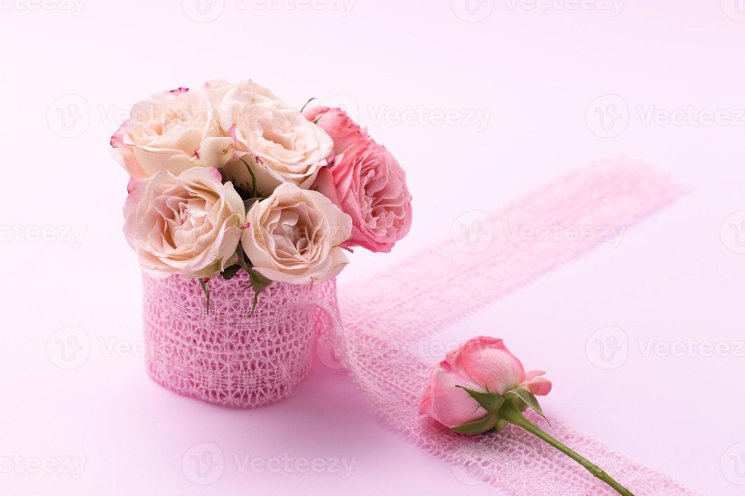 en bukett med vackra rosor står i en liten hink på ett spetsband på en rosa bakgrund med plats för text foto