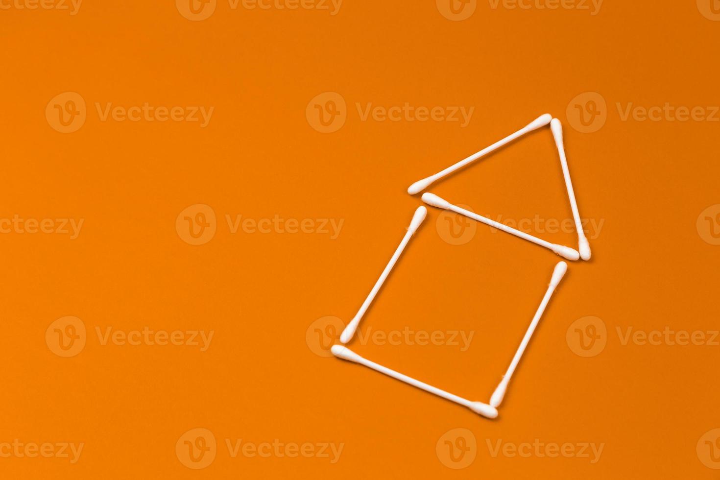 öronpinnar i bomull ordnade som ett litet hus på orange bakgrund foto