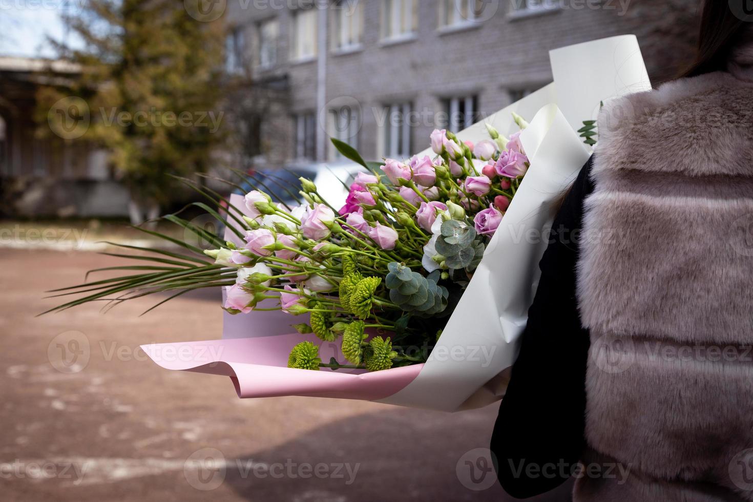 bakifrån av en flicka i en pälsväst som står på gatan som håller en bukett blommor foto